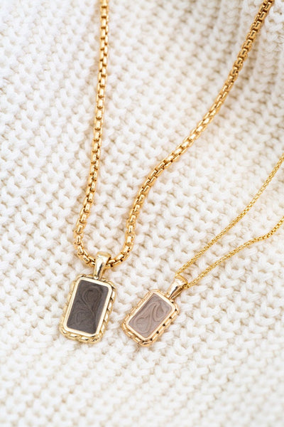 A close-up of Close By Me's Small Cable Cremation Necklace on a thin chain and Medium Cable Cremation Necklace on a thick chain laying on a cream-colored knit material.