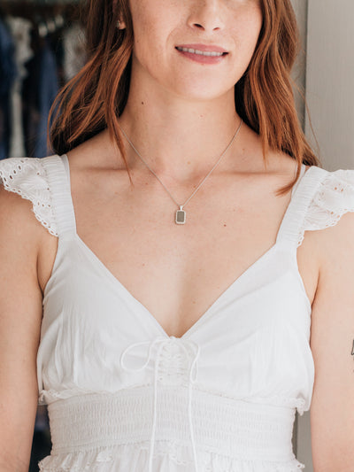 A head-to-waist view of a female, red-haired model in a low-cut white dress wearing Close By Me's Medium Cable Cremation Necklace.