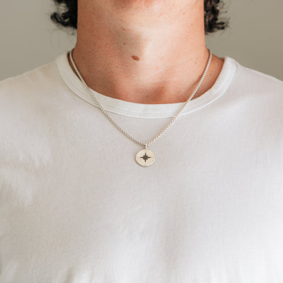 A close-up of a young man wearing Close By Me Jewelry's Compass Cremation Necklace in Sterling Silver on a 2.5mm Sterling Silver chain.