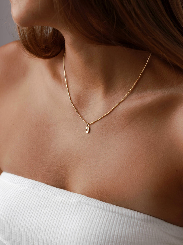 A young woman wears The Guidance Birthstone Charm from Close By Me in 14k yellow gold around her neck.