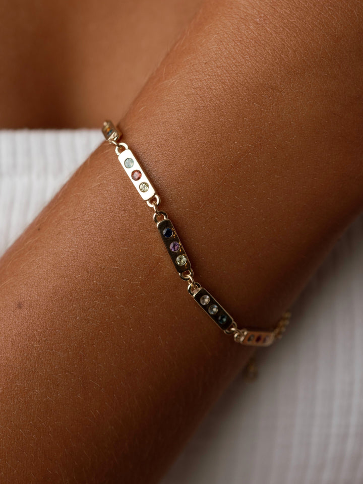 The Tribute Bracelet by Close By Me in 14K Yellow Gold on a model's wrist. It has five links with three different birthstones in each.