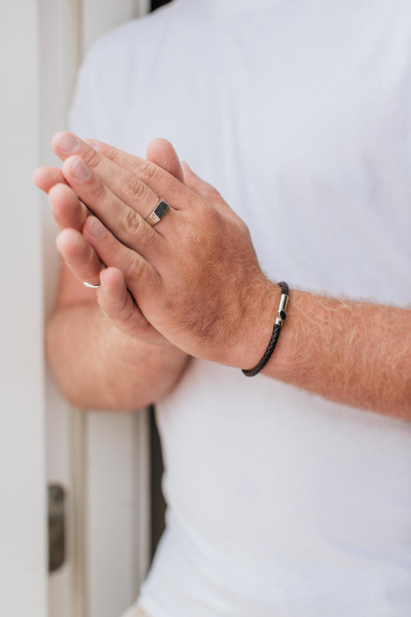 the cremation leather cord bracelet is shown on a male model with his hands clasped together from further away