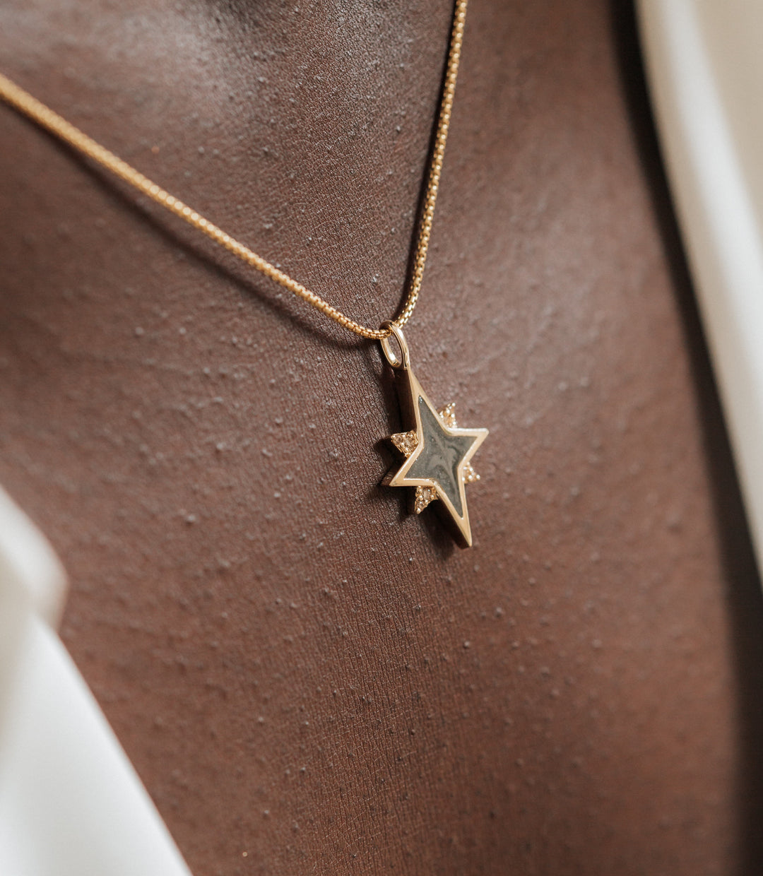 A detailed shot of the North Star Cremation Pendant with Champagne Diamonds in 14K Yellow Gold by close by me jewelry on a model with dark skin