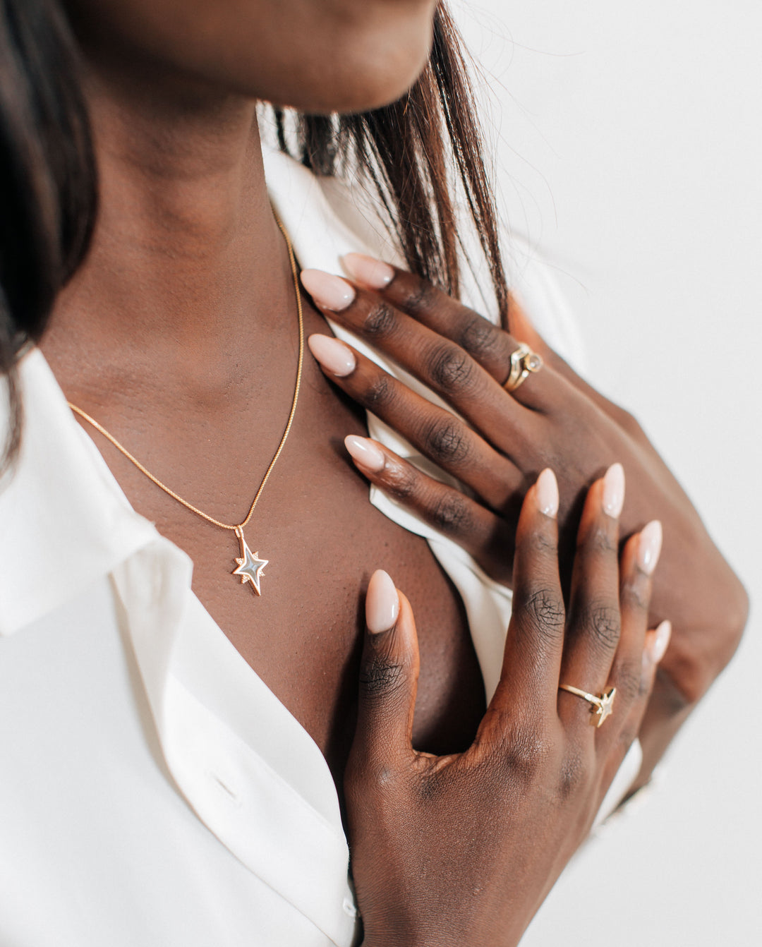 A dark skinned model in a white blouse wearing the North Star Cremation and Champagne Diamond Necklace in 14K Yellow Gold by close by me jewelry