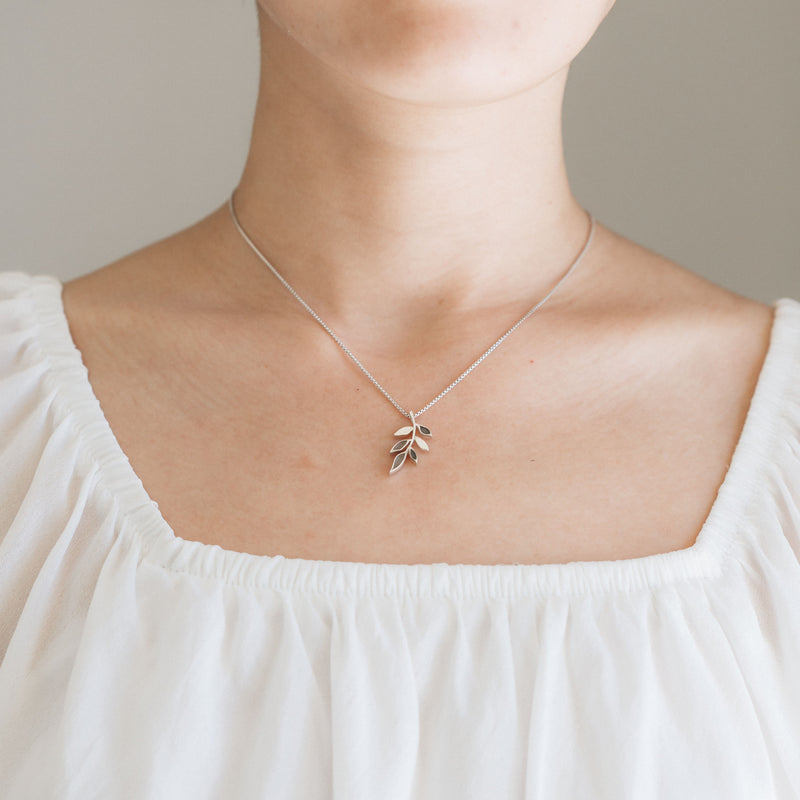 This photo shows a model in a white blouse wearing the Sterling Silver Olive Branch Pendant with cremains by close by me jewelry