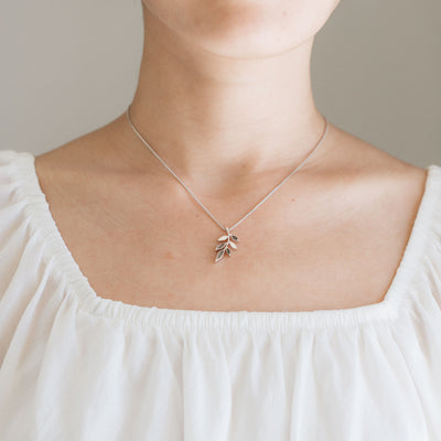 This photo shows a model in a white blouse wearing the Sterling Silver Olive Branch Pendant with ashes by close by me jewelry