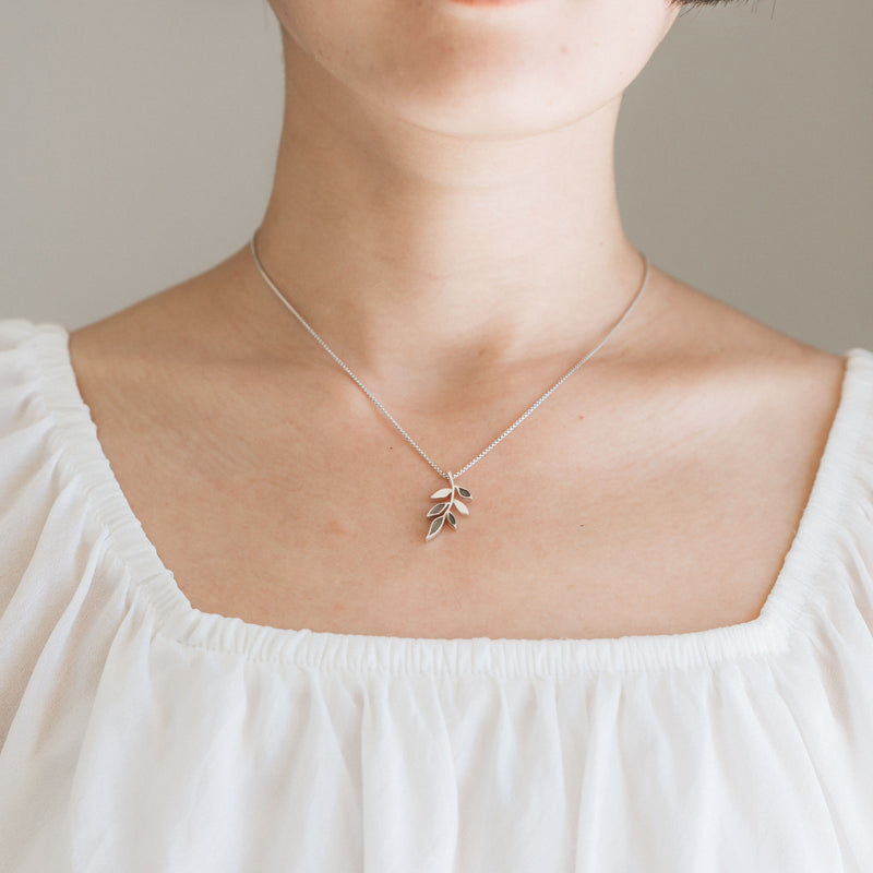 This photo shows a model in a white blouse wearing the Sterling Silver Olive Branch Pendant with ashes by close by me jewelry