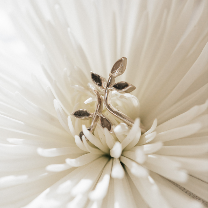 This photo shows the Olive Branch Cremation Ring in Sterling Silver sitting in the petals of a white flower