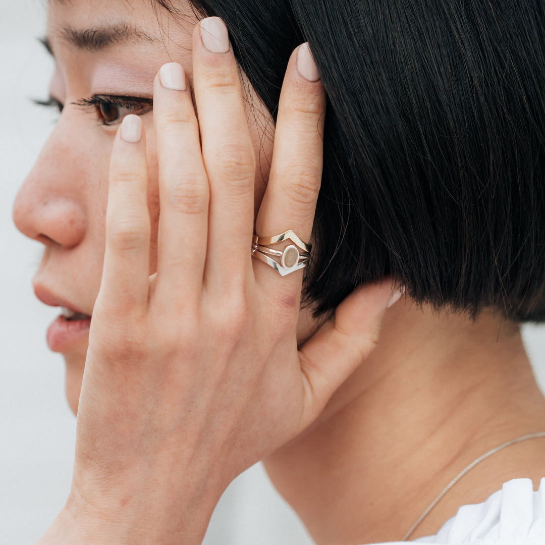 This photo shows a model wearing a Sterling Silver Stacking Ring set designed by close by me jewelry; The Oval Stacking Ring with ashes sits between two Chevron Companion Stacking Rings