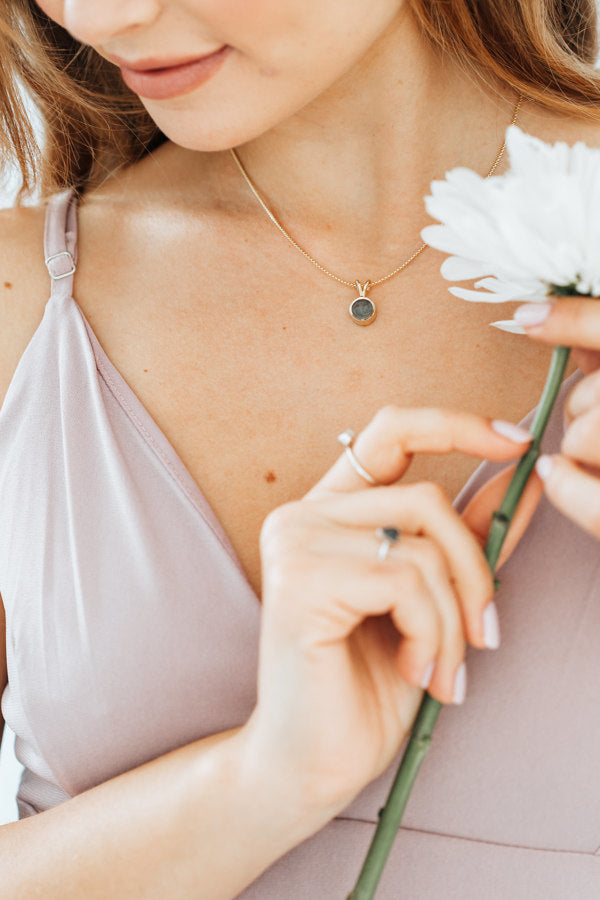 Pictured here is a model in a lavender dress and holding a white flower wearing close by me jewelry's Rabbit Ear Necklace with cremains design in 14K Yellow Gold
