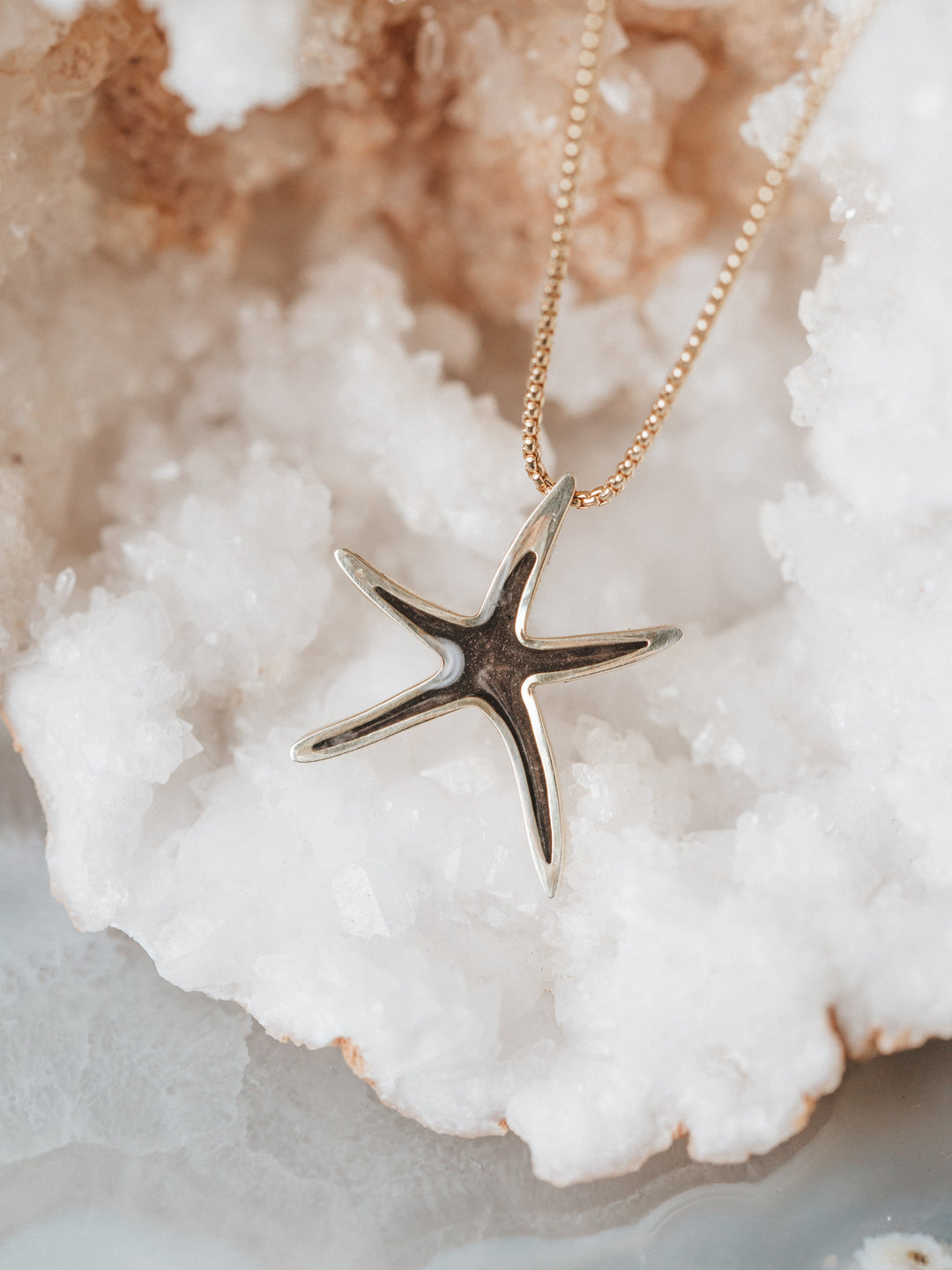 Close-up of Close By Me's Sea Star Cremation Necklace resting on a white and orange-colored crystal cluster.