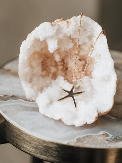 Close By Me's Sea Star Cremation Necklace resting on a white and orange-colored crystal cluster.