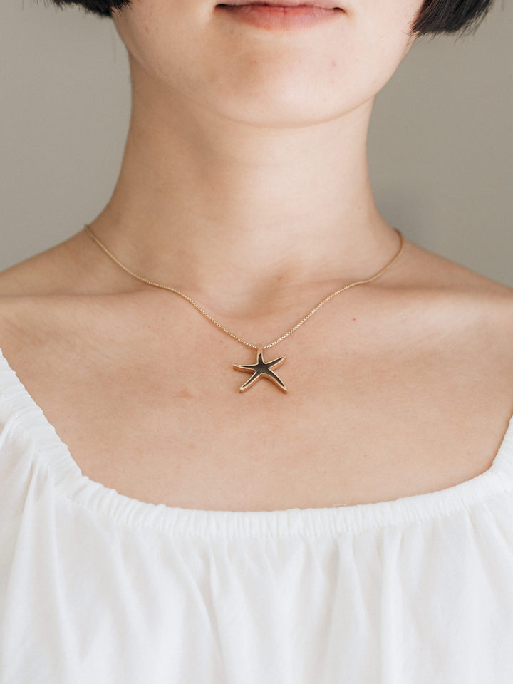 Cropped, close-up view of Close By Me's Sea Star Cremation Necklace being worn around the neck of a female model.
