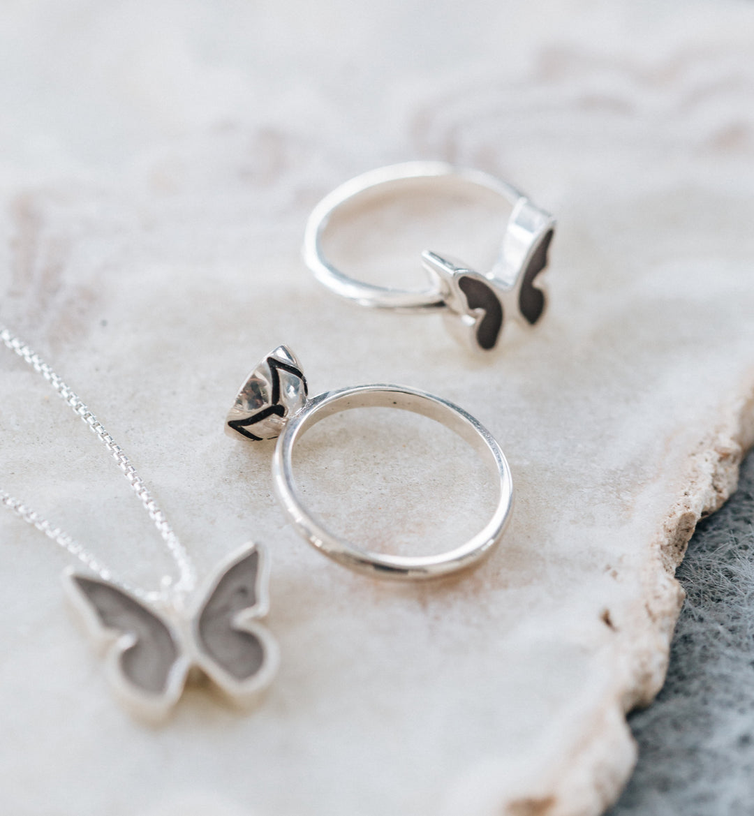 This photo shows a flat-lay of several pieces of cremation jewelry by close by me jewelry, including the Sterling Silver Signature Lotus Stackable Band Cremation Ring with cremated remains