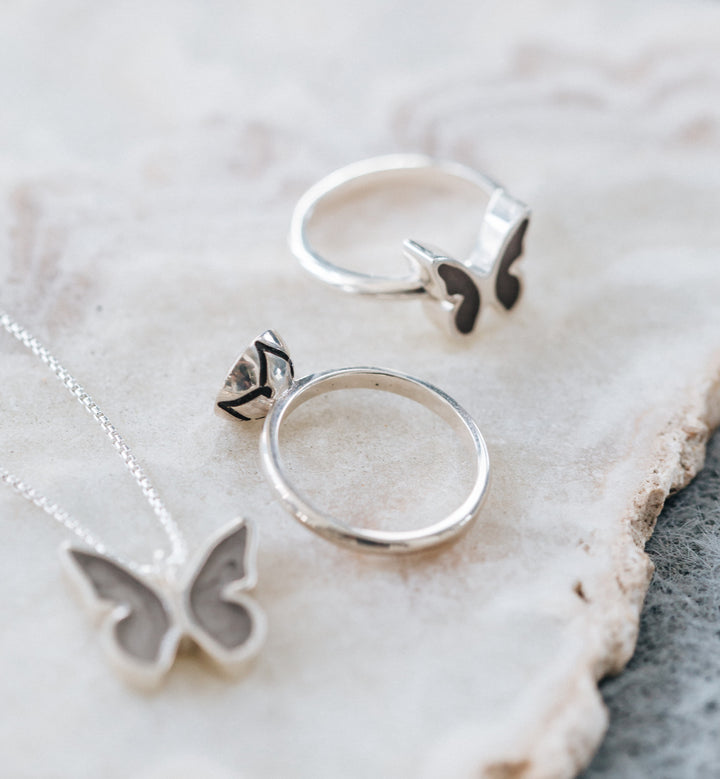 This photo shows a flat-lay of several pieces of cremation jewelry by close by me jewelry, including the Sterling Silver Signature Lotus Stackable Band Cremation Ring with cremated remains