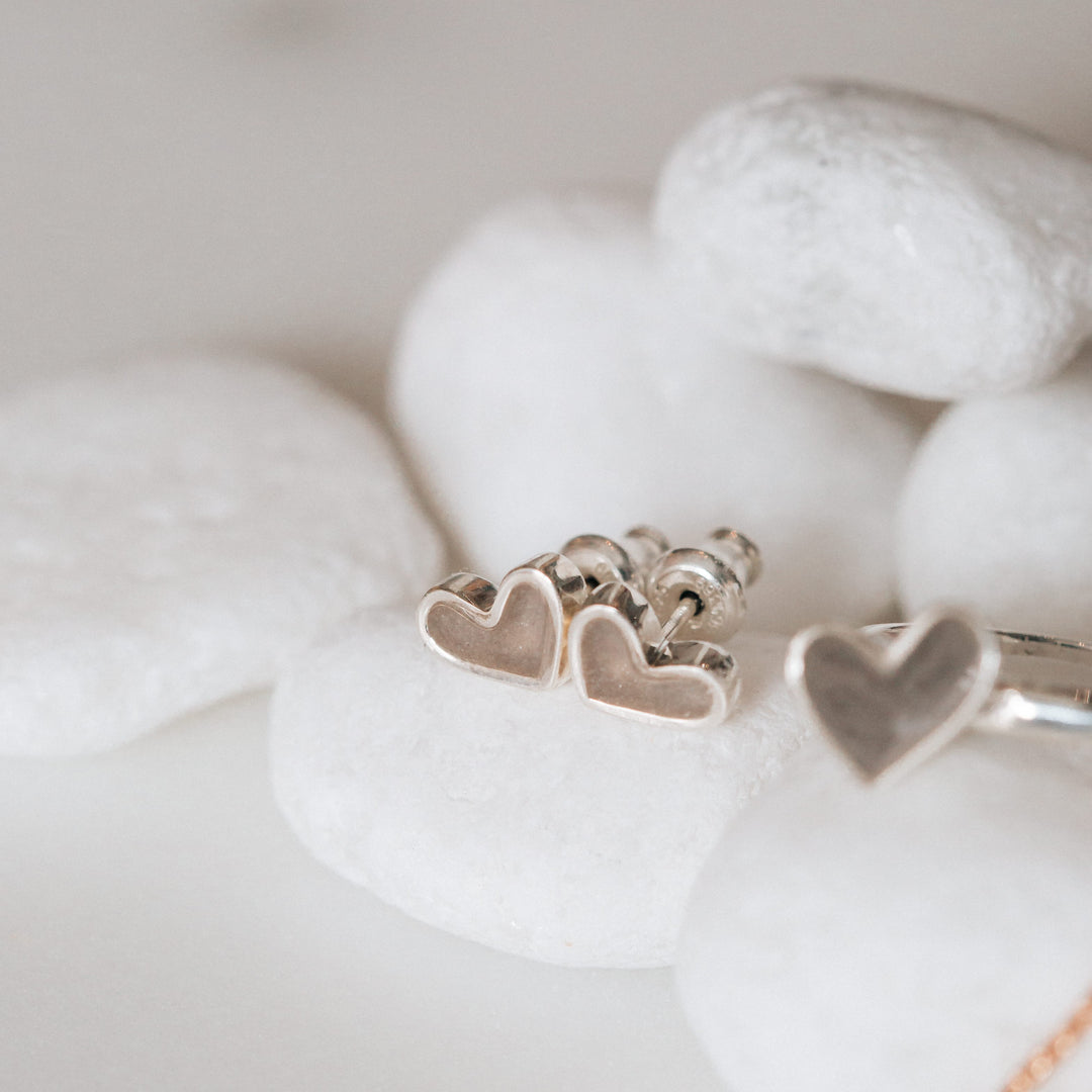Signature heart stud cremation earrings in 14k white gold shown as a flatlay on a pile of white rocks