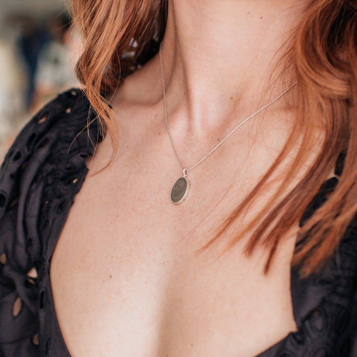 A light-skinned model with red hair wearing the simple bail oval ashes necklace by close by me jewelry
