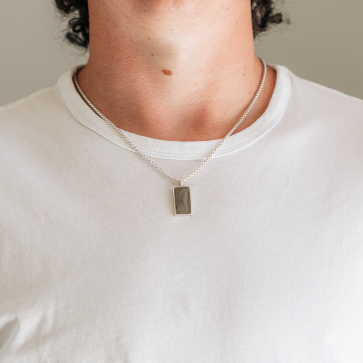 A male model with light skin in a white t-shirt wearing close by me jewelry's simple bail rectangle men's memorial necklace in sterling silver