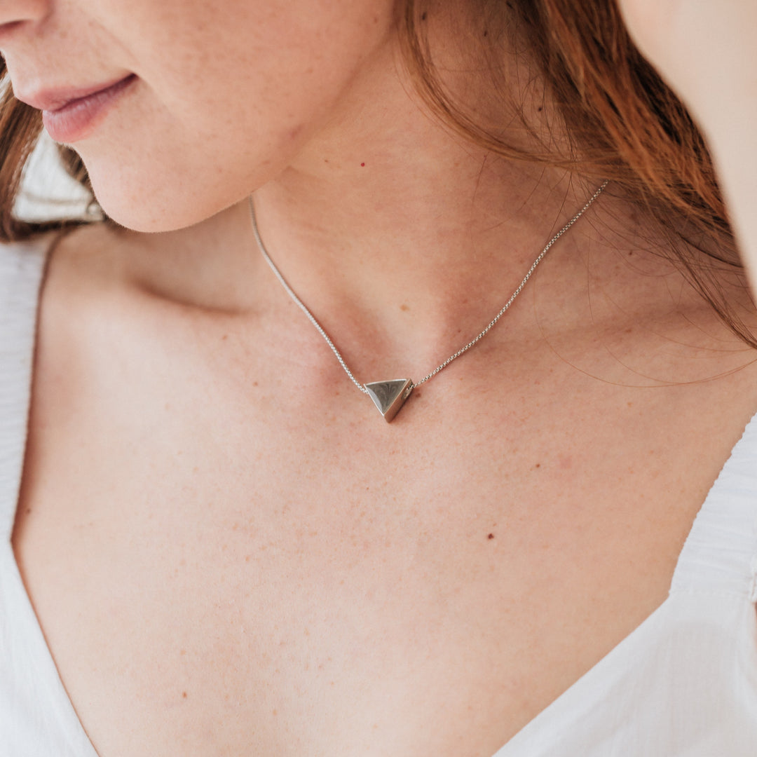 The Sterling Silver Ashes Necklace with a Sliding Triangle setting by close by me jewelry around a light skinned, red-haired model's neck 