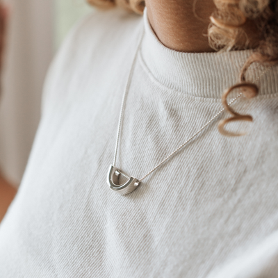 A close up showing the sliding "u" pendant with ashes designed in sterling silver by close by me jewelry around a model's neck