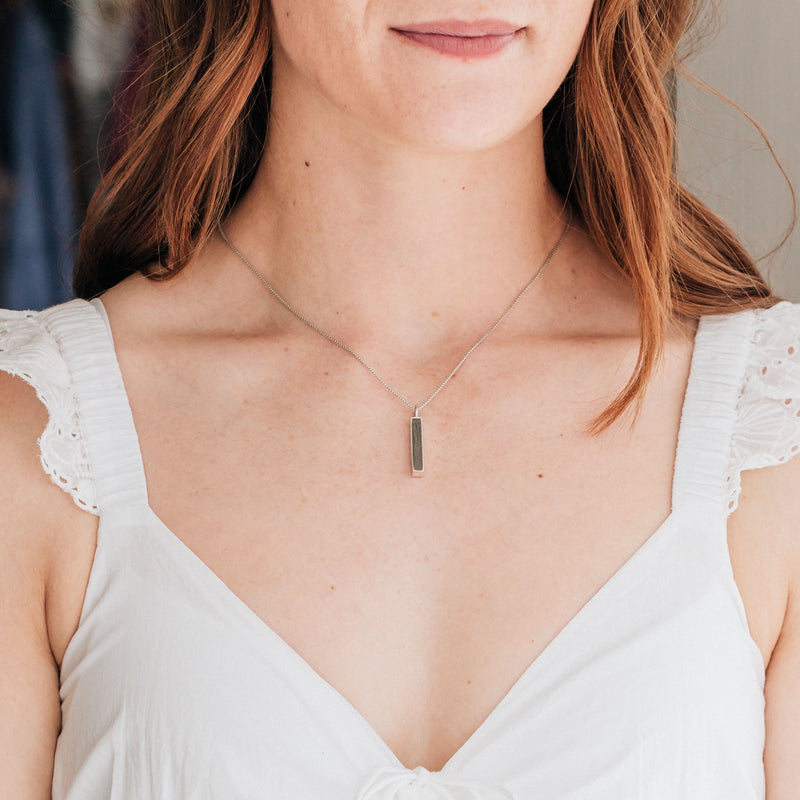 The small bar pendant with ashes in sterling silver designed by close by me jewelry being worn by a model in a white dress