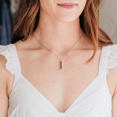 The small bar necklace with cremated remains in sterling silver designed by close by me jewelry being worn by a model in a white dress