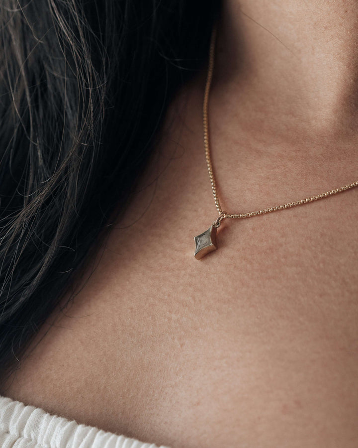 A close up photo of a model in close by me's 14k rose gold ashes necklace shaped like a small diamond