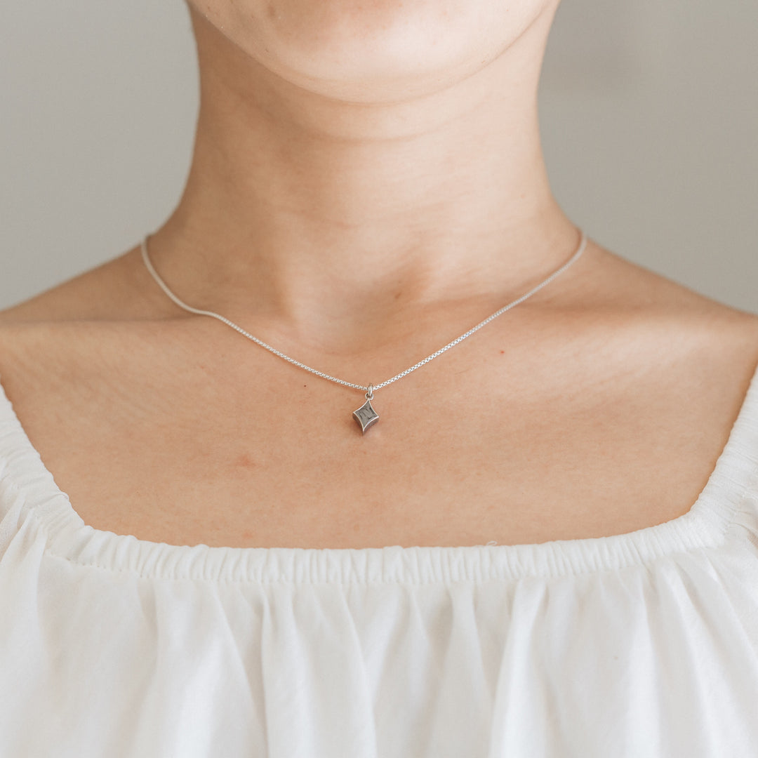 Pictured here is close by me jewelry's Small Diamond Charm with Cremated Remains in Sterling Silver being worn by a light skinned model in a white top
