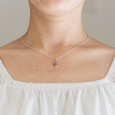 Pictured here is close by me jewelry's Small Diamond Charm with Cremated Remains in Sterling Silver being worn by a light skinned model in a white top