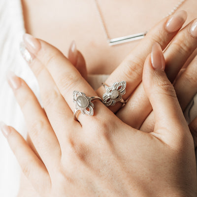 A close-up of a female model's hands crossed against her chest. On her left index finger is Close By Me's Large Setting World War II Cremation Ring; on her right is Close By Me's Small Setting World War II Cremation Ring.