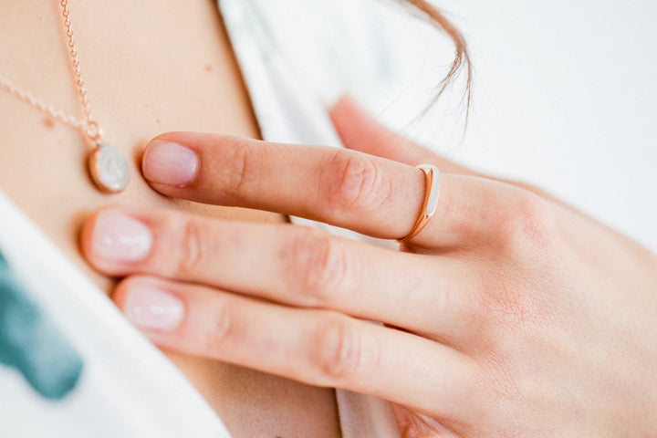A close up photo showing a model in a white dress wearing close by me jewerly's smooth band ring with ashes