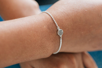 A tan model wearing a grey sweater shows the bolo chain bracelet in sterling silver on her arm more close up