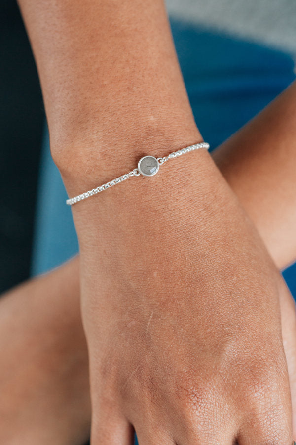 A tan model wearing a grey sweater shows the bolo chain bracelet in sterling silver on her arm