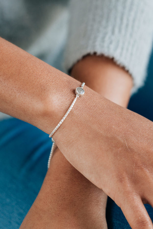 A tan model wearing a grey sweater shows the bolo chain bracelet in sterling silver on her wrist.