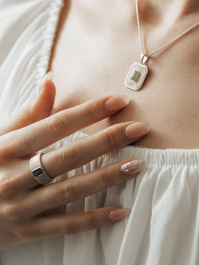 A model, wearing both Close By Me's Tessa Cremation Ring and Tessa Cremation Necklace, rests her hand gently against her chest.