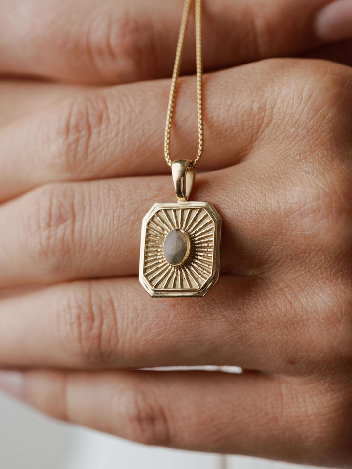 close by me's tessa cremation pendant with oval ashes setting in 14k yellow gold being held up with model's hands