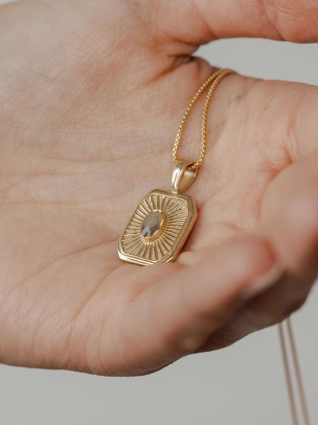 close by me's tessa cremation pendant with oval ashes setting in 14k yellow gold being held in model's hand