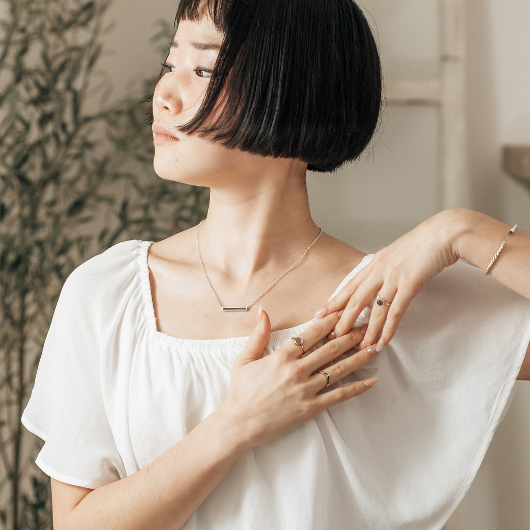 A young woman wearing the thin lateral bar pendant in sterling silver memorial piece while she is gently posing her arms and looking to the side