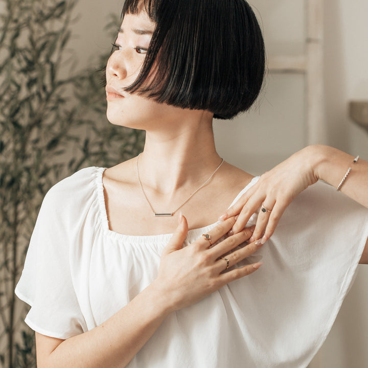 A photo showing a model wearing many pieces of cremation jewelry, including the silver ashes necklace thin lateral bar design