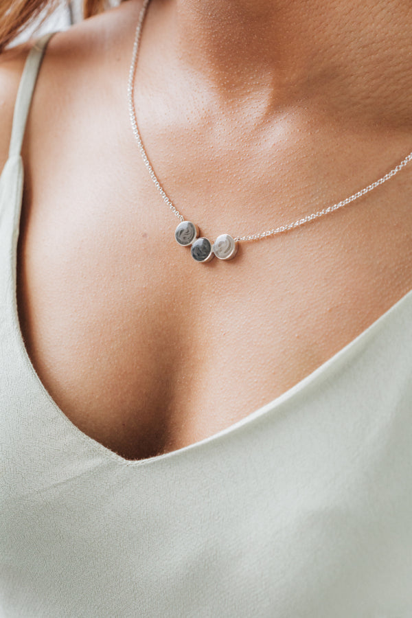 A close up featuring the Three Setting Chevron Cremains Necklace in Sterling Silver around a model's neck