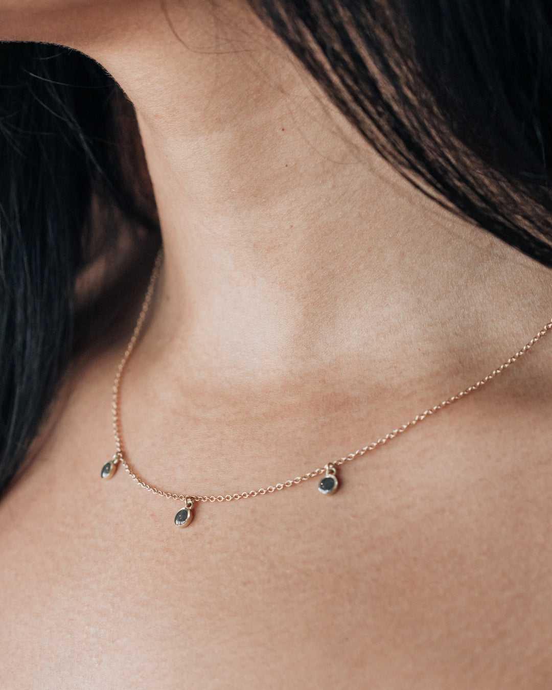 an angled close up of a model wearing a dainty memorial drop cremation necklace by close by me jewelry