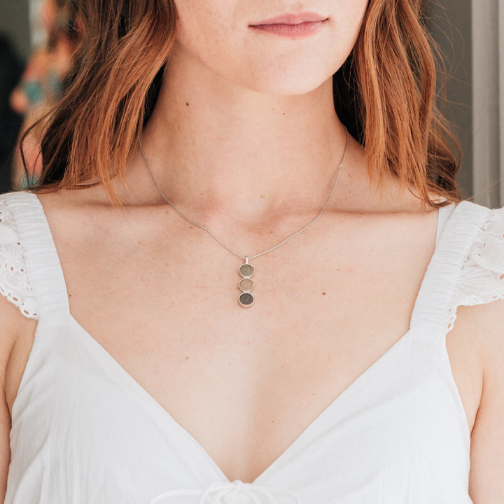 A model in a white dress with red hair wearing close by me jewelry's Triple Setting Circle Cremains Necklace in Sterling Silver