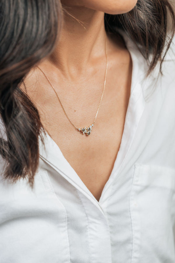 Pictured here is a model with dark hair in a white button-down wearing the 14K Yellow Gold White Sapphire Cluster Pendant with cremains, designed by close by me jewelry