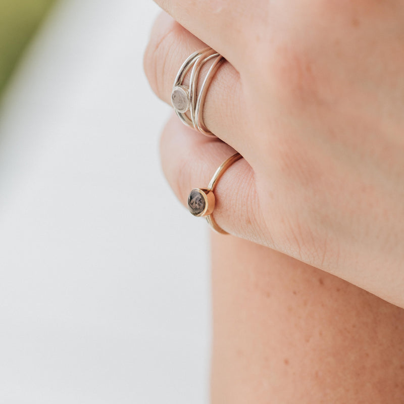 Pictured here is a close up of a model wearing several cremation rings by close by me jewelry. On her pinky, she wears the 5mm Circle Stacking Ashes Ring in 14K Rose Gold.