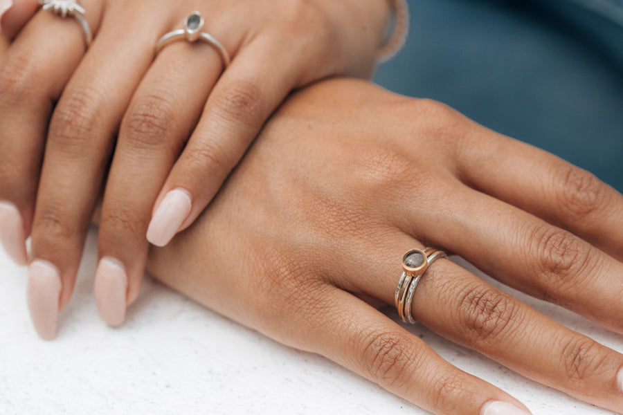 This photo shows a model lying her hand flat while wearing a 14K Rose Gold 5mm Circle Stacking Cremation Ring Set with two Sterling Silver Companion Bands