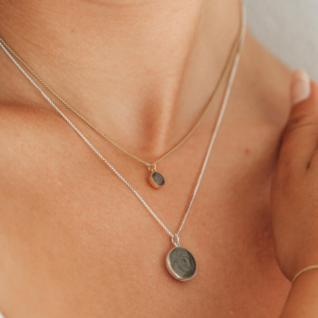 This photo shows a close up of a model wearing two sizes of close by me jewelry's dome pendant series around her neck; the pendant on the shorter chain is the 14K Yellow Gold 6mm Dome Cremains Necklace