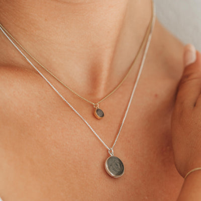 This photo shows a close up of a model wearing two sizes of close by me jewelry's dome pendant series around her neck; the pendant on the shorter chain is the 14K Yellow Gold 6mm Dome Cremains Necklace