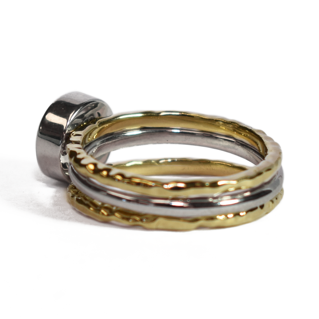 This photo shows a stacking cremation ring set from close by me jewelry from the back and at an angle. The Cremains Ring is an 8mm Circle Stacking Ring in Sterling Silver between two 14K Yellow Gold Textured Companion Rings