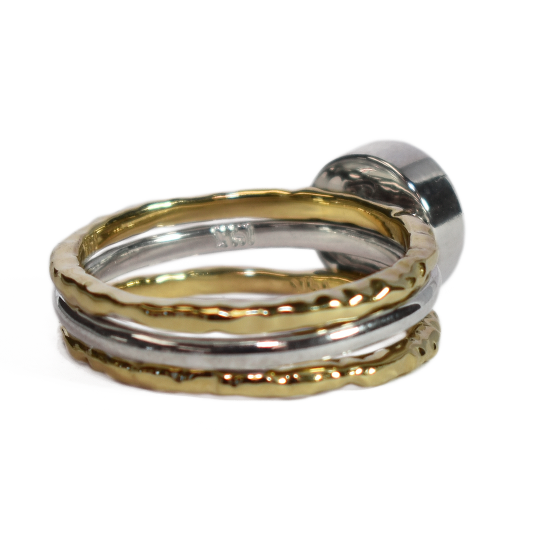 This photo shows a stacking cremation ring set from close by me jewelry from the back and at a slight angle. The Cremains Ring is an 8mm Circle Stacking Ring in Sterling Silver between two 14K Yellow Gold Textured Companion Rings