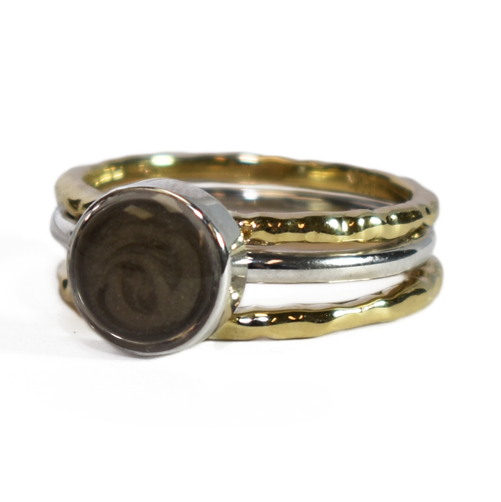 This photo shows a stacking cremation ring set from close by me jewelry at a slight angle. The Cremains Ring is an 8mm Circle Stacking Ring in Sterling Silver between two 14K Yellow Gold Textured Companion Rings